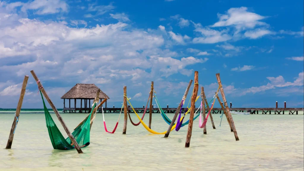 Hamacas coloridas sobre el agua turquesa de Holbox bajo un cielo azul con nubes