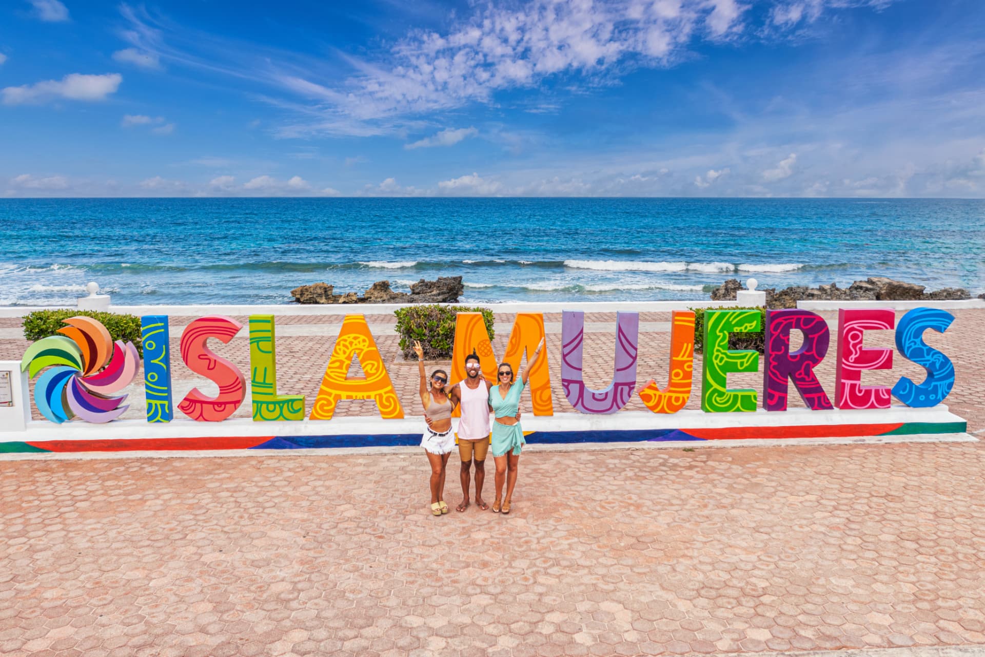 Letrero colorido de Isla Mujeres frente al mar con turistas celebrando